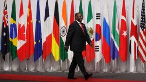Cyril Ramaphosa walking on a red carpet past a long line of G20 national flags, including South Africa