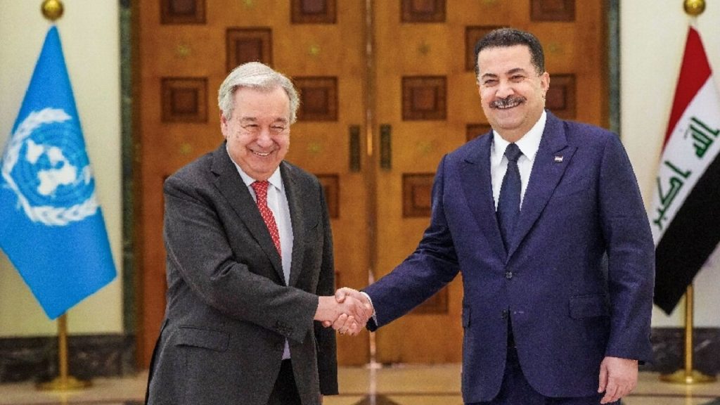 United Nations Secretary-General António Guterres shaking hands with Iraqi Prime Minister Mohammed Shia' al-Sudani in front of UN and Iraqi flags
