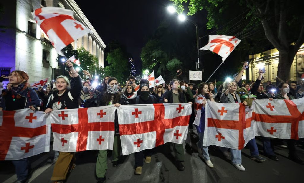 Large group of protesters holding up the red and white flag of Georgia during a nighttime demonstration on a city street