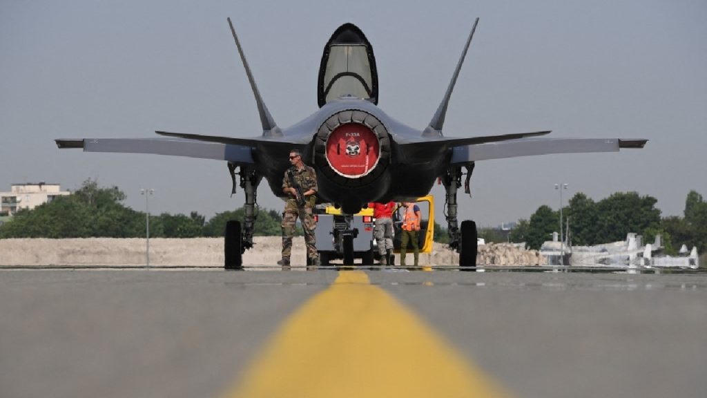 A U.S. F-35 Lightning II stealth fighter jet flying in the sky, with the Turkish flag blurred in the foreground