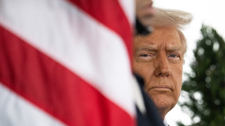 Close-up of Donald Trump's face partially obscured by the American flag's red stripes, focusing on his serious expression