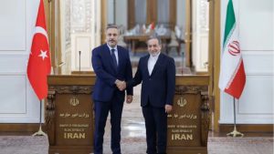 Turkish and Iranian officials shaking hands in a formal setting, flanked by the flags of Turkey and Iran