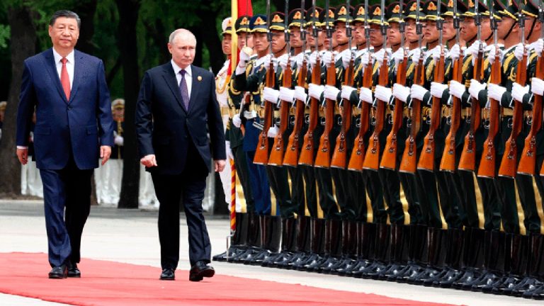 Xi Jinping and Vladimir Putin walking side-by-side past a long line of Chinese soldiers standing at attention with rifles.