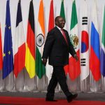 Cyril Ramaphosa walking on a red carpet past a long line of G20 national flags, including South Africa