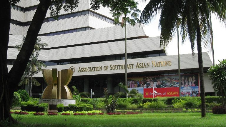 The exterior of the Association of Southeast Asian Nations (ASEAN) headquarters building with lush green landscaping and the "Symbol of Unity" monument.