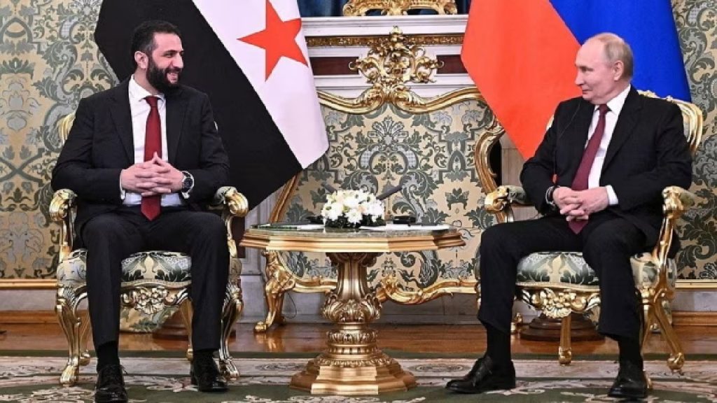Vladimir Putin seated across a table from a Syrian official, in a formal meeting setting with flags in the background