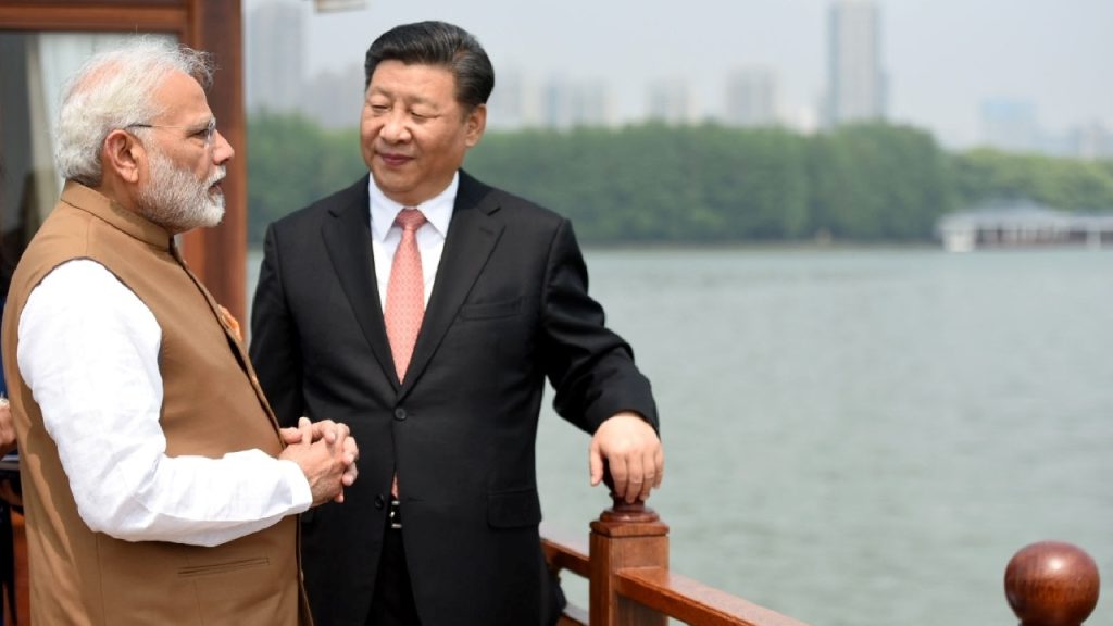 Narendra Modi and Xi Jinping engaged in a conversation while standing on a wooden boat or deck with a lake and greenery in the background.