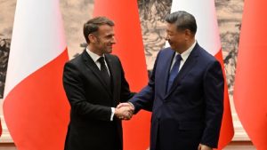 French President Emmanuel Macron and Chinese President Xi Jinping shaking hands and smiling warmly in front of national flags.