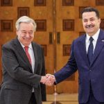 United Nations Secretary-General António Guterres shaking hands with Iraqi Prime Minister Mohammed Shia' al-Sudani in front of UN and Iraqi flags