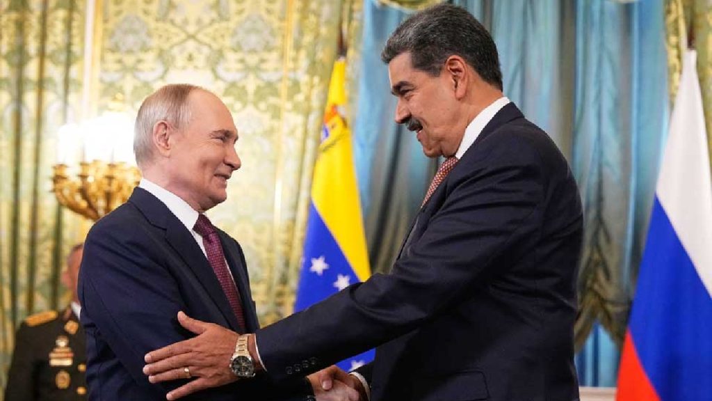 Vladimir Putin and Nicolas Maduro shaking hands and smiling in a formal, gold-decorated room with national flags.