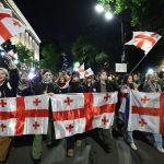 Large group of protesters holding up the red and white flag of Georgia during a nighttime demonstration on a city street