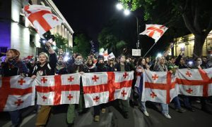 Large group of protesters holding up the red and white flag of Georgia during a nighttime demonstration on a city street