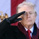 Donald Trump wearing a black overcoat, leather gloves, and a red scarf, delivering a military salute outdoors