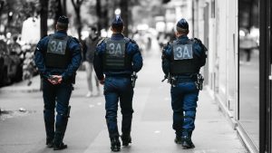 Three police officers in navy blue uniforms with "3A" patches on their backs walking down a city street