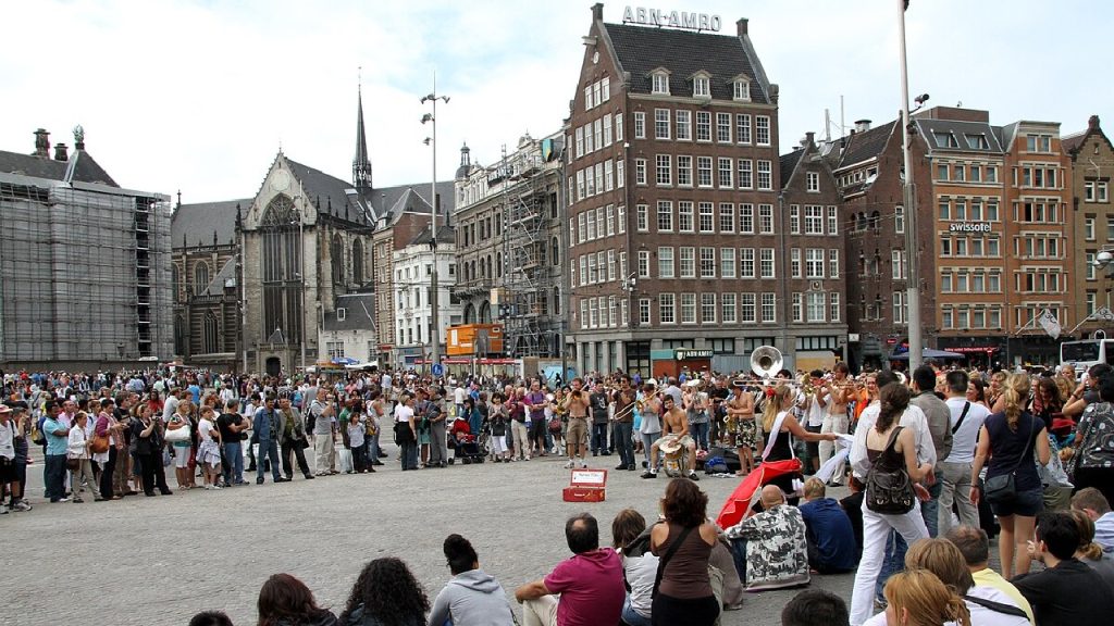 Busy city square in Amsterdam with historic buildings, crowded with locals and tourists, and street performers