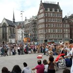 Busy city square in Amsterdam with historic buildings, crowded with locals and tourists, and street performers