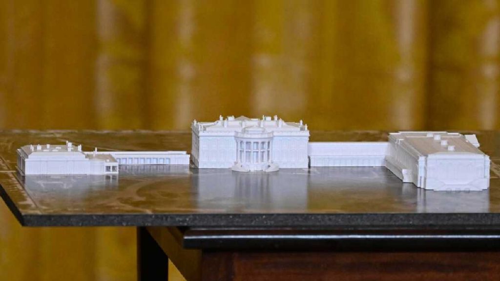 A detailed white 3D-printed scale model of the White House including the East and West wings, placed on a dark table.