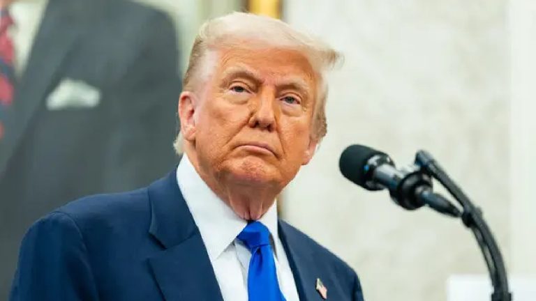 Close-up portrait of Donald Trump looking contemplative during a press conference with a microphone in the foreground.