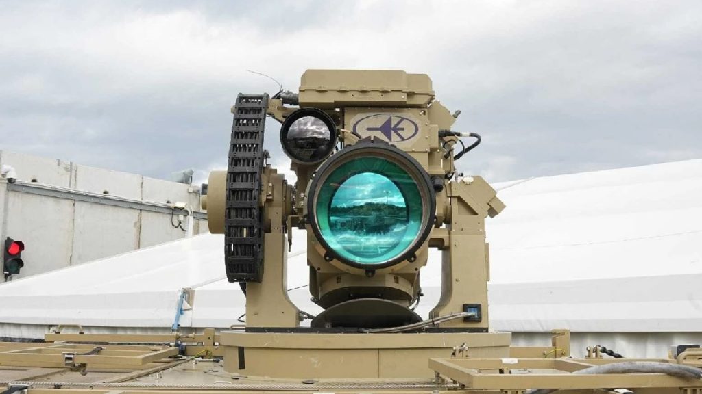 A sophisticated tan-colored laser or optical weapon system mounted on a platform.