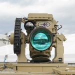 A sophisticated tan-colored laser or optical weapon system mounted on a platform.