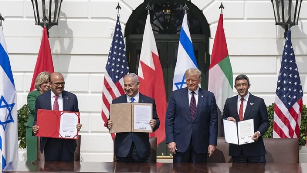 Four world leaders standing outdoors in front of international flags, holding signed documents.