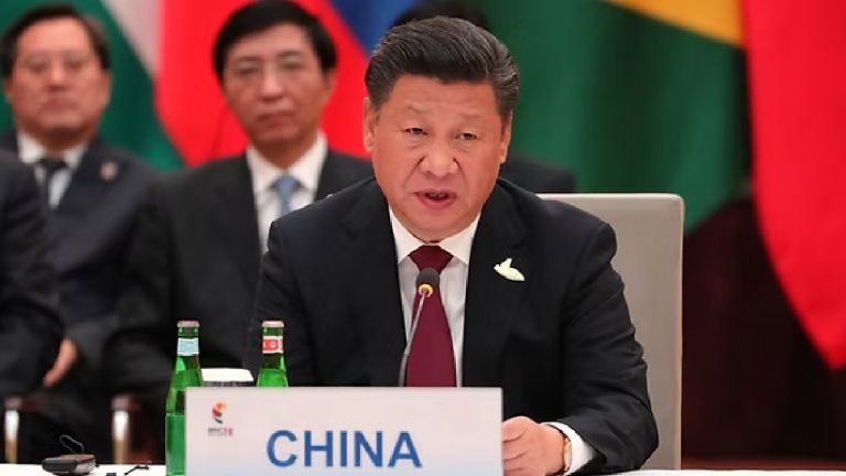 Xi Jinping speaking at a conference with a "CHINA" nameplate in front of him and international flags in the background.