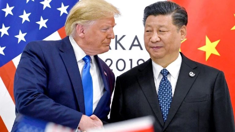 US President Donald Trump and Chinese President Xi Jinping shaking hands during a formal meeting, both wearing dark suits with red and blue ties against a backdrop of national flags.