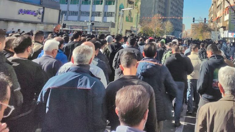 A large crowd of people walking down a city street, viewed from behind.