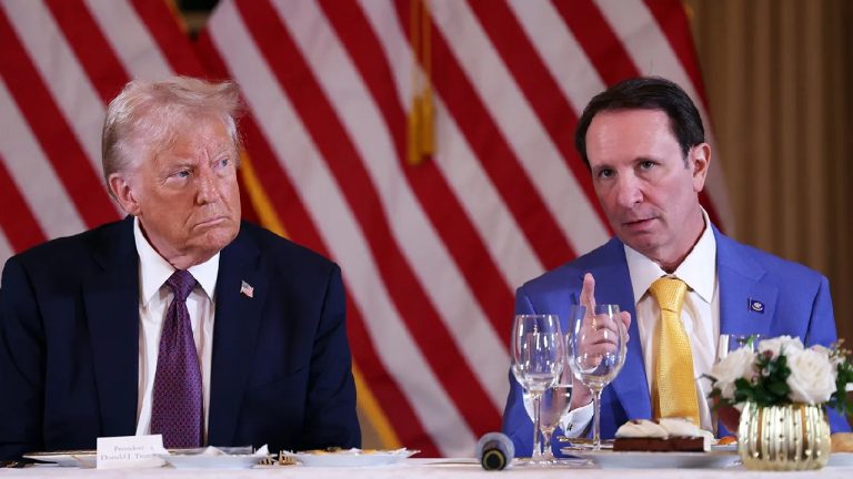Donald Trump and Jeff Landry sitting at a formal dinner table with American flags in the background.