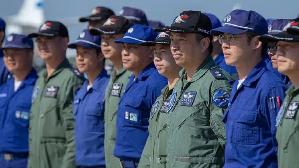 A group of military personnel in blue and green flight suits standing in formation.