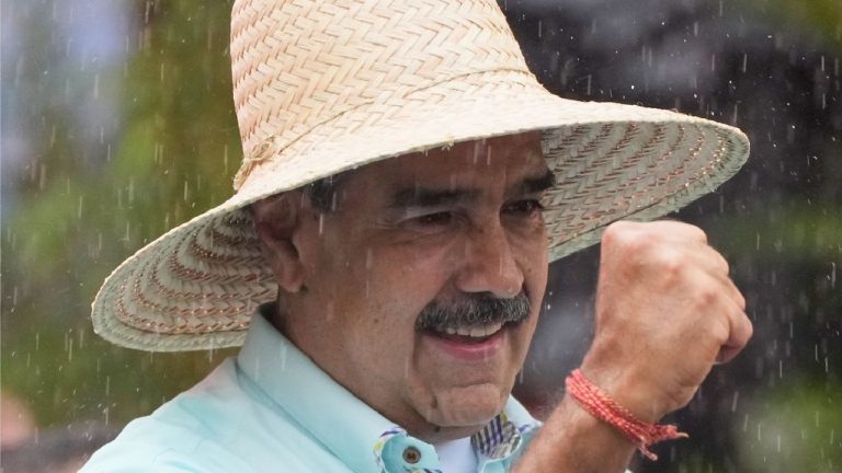Close-up of a smiling man with a mustache wearing a wide-brimmed straw hat and a light blue shirt.
