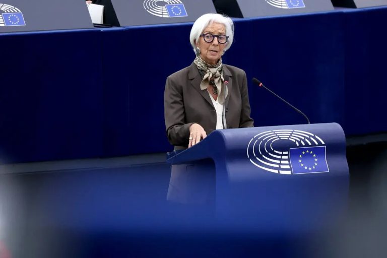 A close-up portrait of Christine Lagarde speaking at a podium, wearing a dark blue suit and a patterned scarf, with a large blue background featuring a yellow "msc" logo and the text "Munich Security Conference."