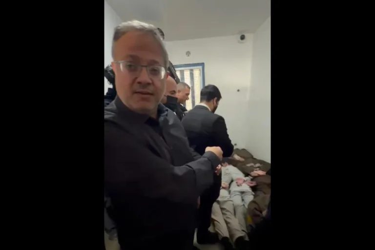 Israeli National Security Minister Itamar Ben-Gvir standing inside a prison facility with several Palestinian detainees lying on the floor in the background.
