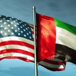 The national flags of the United States of America and the United Arab Emirates flying side-by-side against a blue sky with soft clouds.