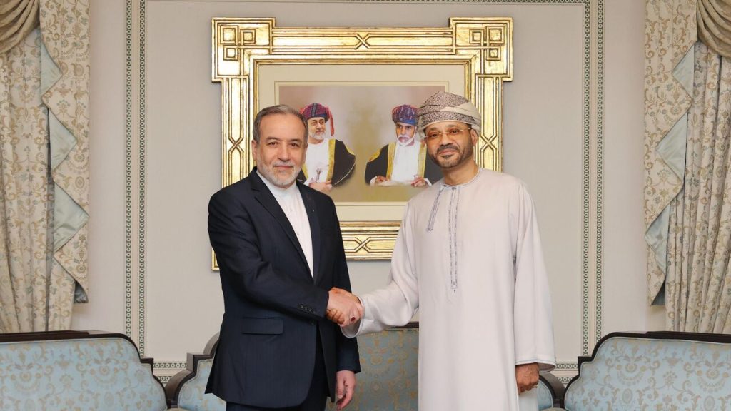 Two men in formal attire, Abbas Araghchi in a dark suit and Sayyid Badr Albusaidi in traditional Omani dress, shaking hands in a formal room in front of a framed portrait of Omani leaders.