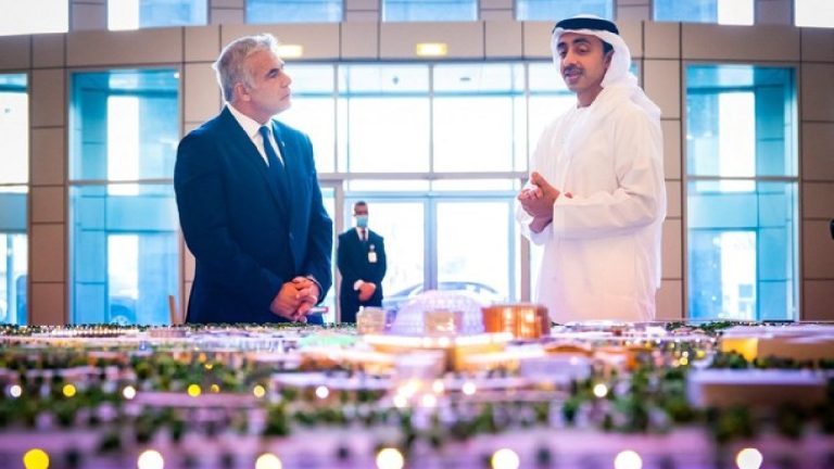 Two men in formal attire standing in a modern hall, looking at a large architectural model of a city.