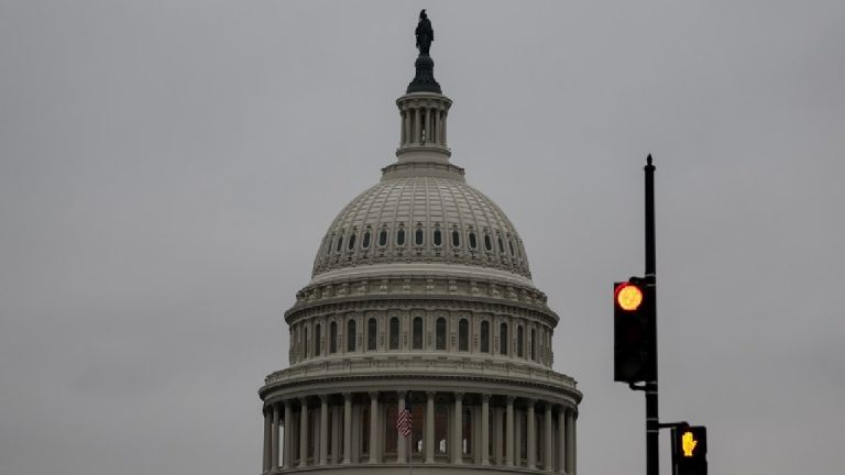 The dome of the United States Capitol building under a gray sky with a red traffic light in the foreground.