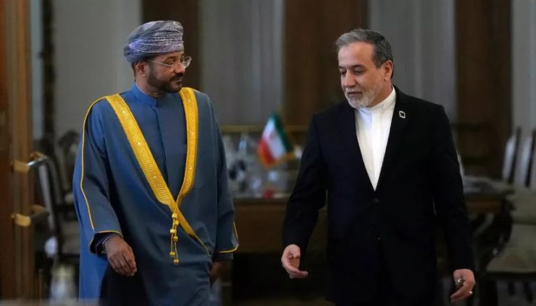 A medium shot of Iranian Foreign Minister Abbas Araghchi and Omani Foreign Minister Sayyid Badr Albusaidi standing together in a formal indoor setting, both smiling slightly at the camera.