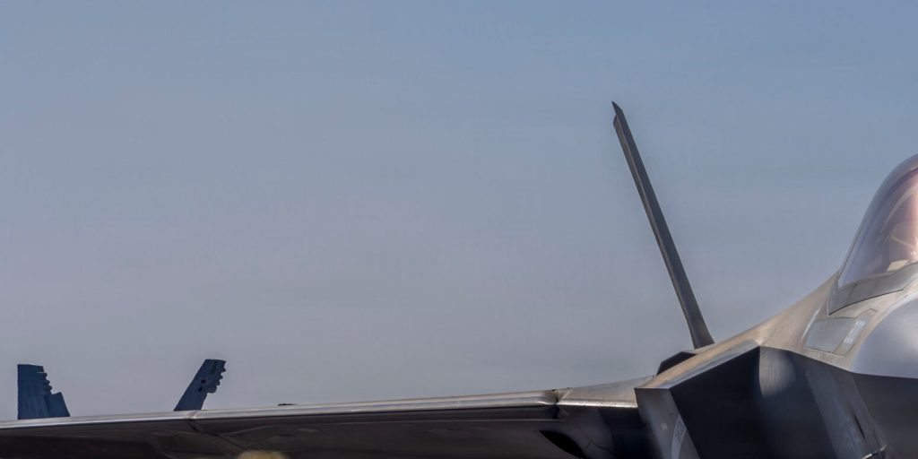 Close-up of an F-35 stealth fighter jet wing and tail against a clear sky.