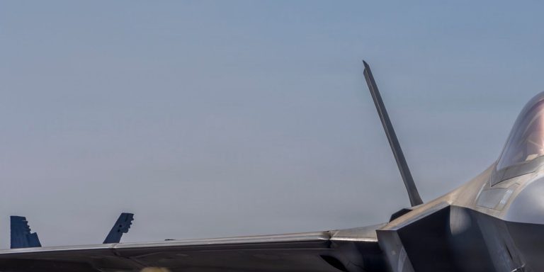 Close-up of an F-35 stealth fighter jet wing and tail against a clear sky.