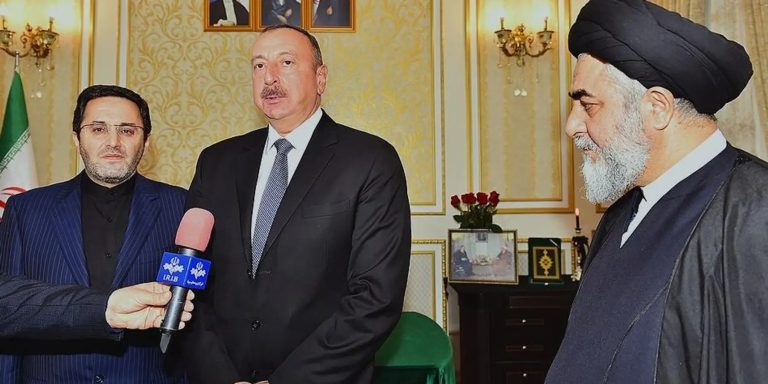 President Ilham Aliyev of Azerbaijan standing with an Iranian cleric and an official during a press meeting.