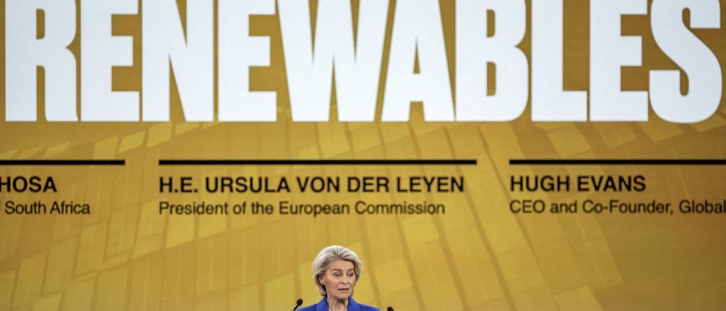 Ursula von der Leyen speaking at a podium with a large "RENEWABLES" sign in the background.