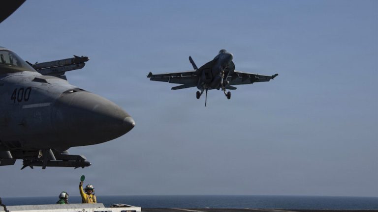 Massive ruins of ancient Egyptian statues, including colossal stone feet and a partially standing obelisk under a bright blue sky.