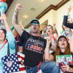 A crowd of supporters at a rally, with a man in a "Persians for Trump" t-shirt shouting and raising his fist.