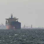 A large oil tanker ship sailing on choppy ocean waters under a hazy sky with other vessels in the distance.