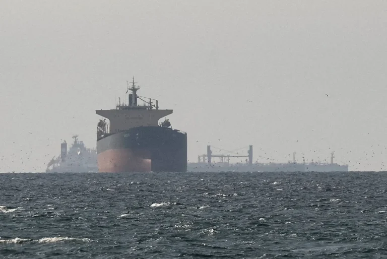A large oil tanker ship sailing on choppy ocean waters under a hazy sky with other vessels in the distance.