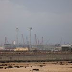 A vast industrial natural gas processing facility under a hazy sky with numerous cranes and storage tanks.