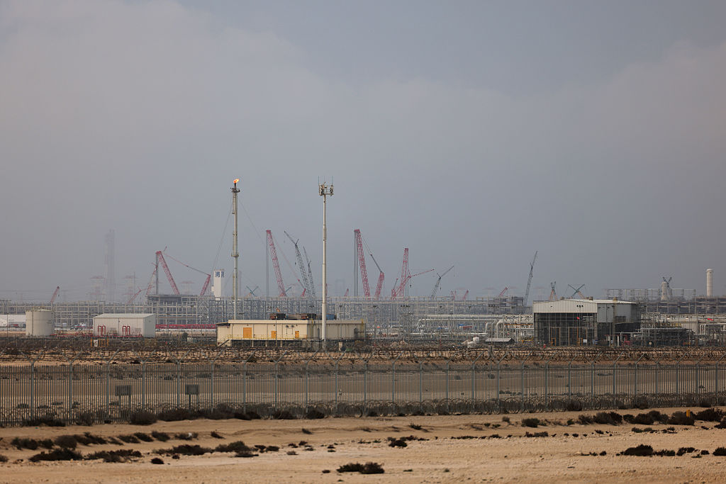 A vast industrial natural gas processing facility under a hazy sky with numerous cranes and storage tanks.