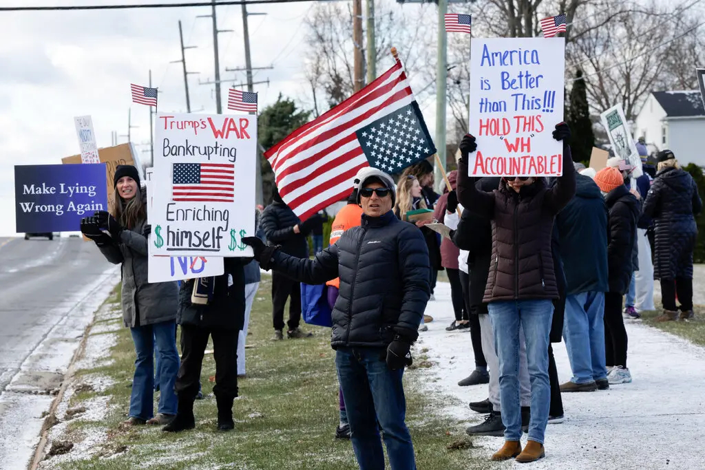 Protesters holding signs and American flags during a political demonstration on a snowy roadside, featuring placards with slogans like "Make Lying Wrong Again" and "Hold This WH Accountable."