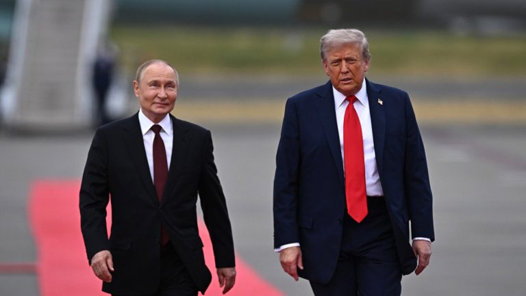 Vladimir Putin and Donald Trump walking side-by-side on an airport tarmac next to a red carpet.